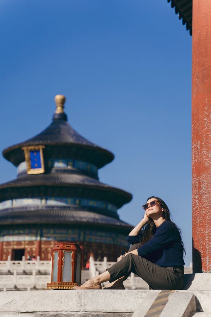 Mujer con gafas de sol sentada en un patio de piedra frente a la pagoda del Templo del Cielo en Pekín, China.