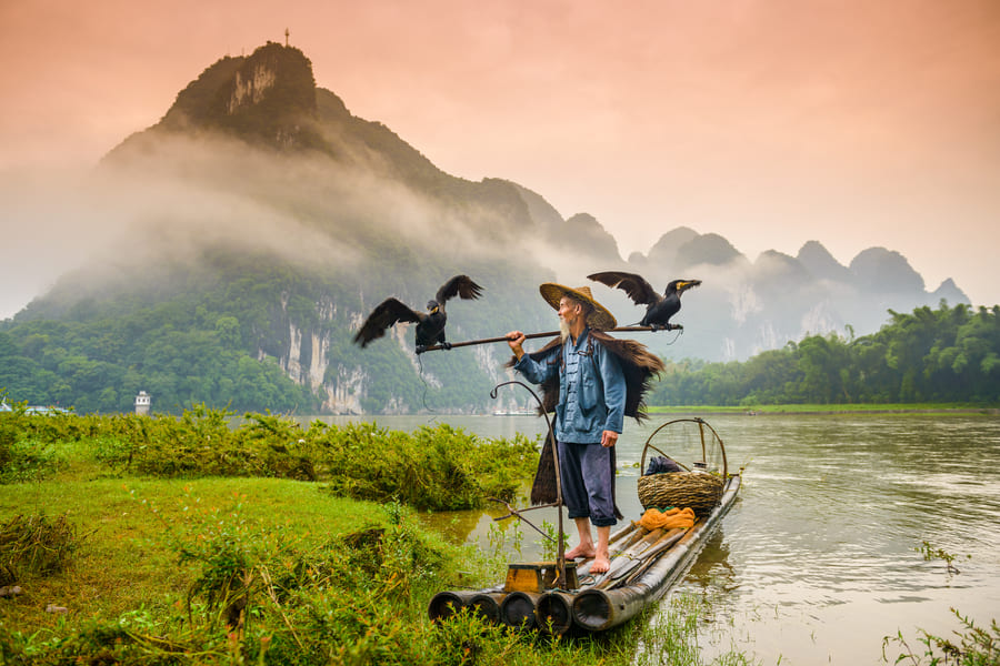 Pescador tradicional chino con cormoranes en una balsa de bambú en el río Li, Yangshuo, ante montañas de karst con niebla.